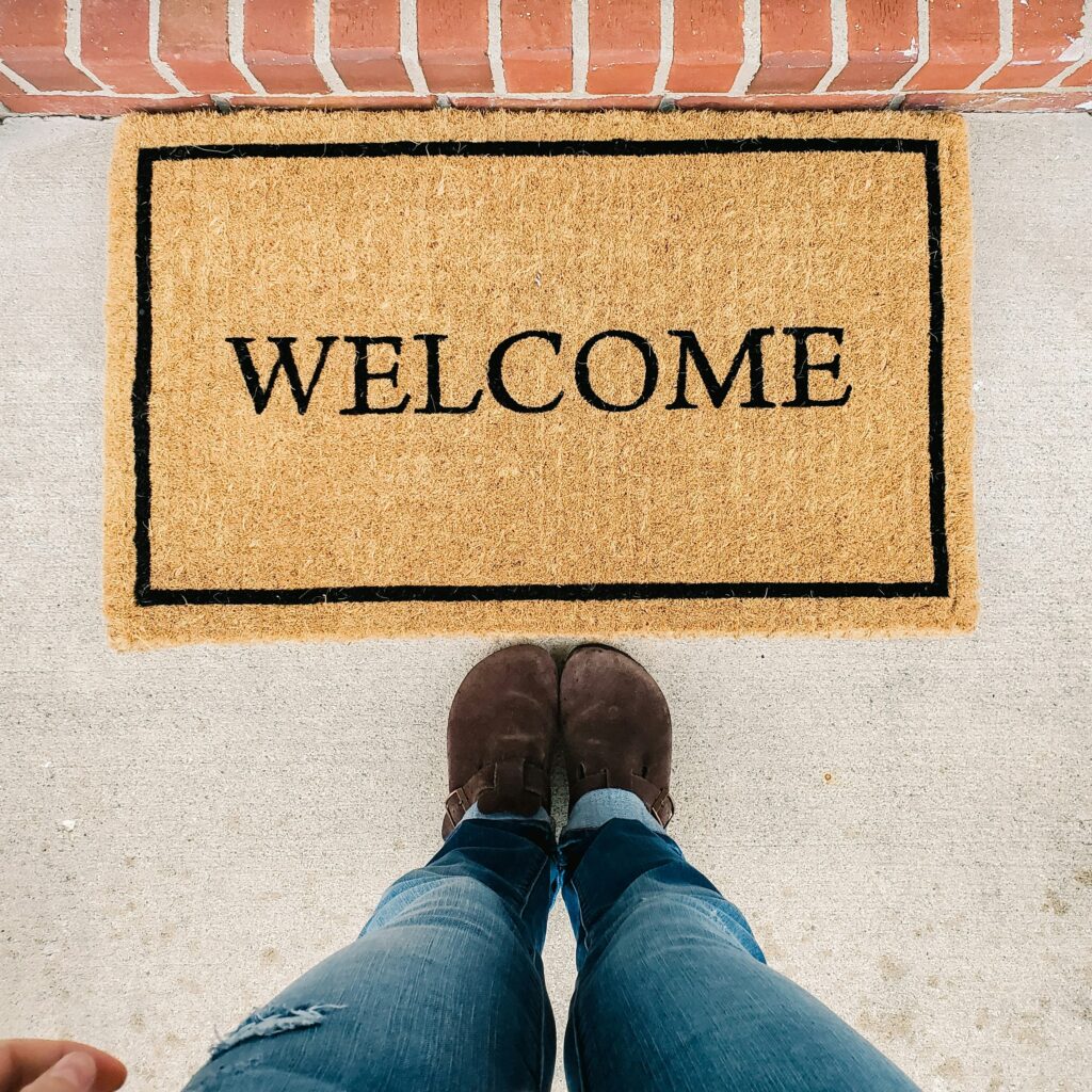 A photo from the perspective of a person showing their legs and a welcome mat.
