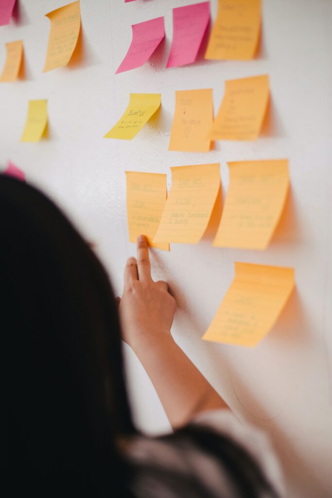 A photo showing post-it notes on a white board with someone pointing.