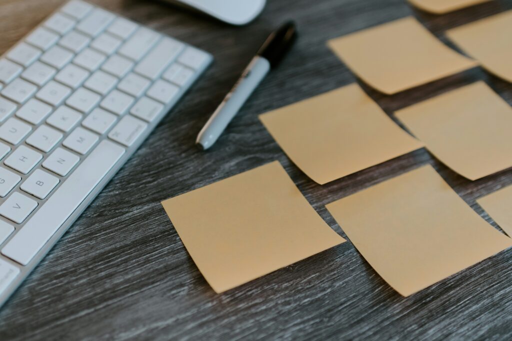 A photograph of blank orange post-it notes arranged in a diagonal line, next to a keyboard and black marker pen.