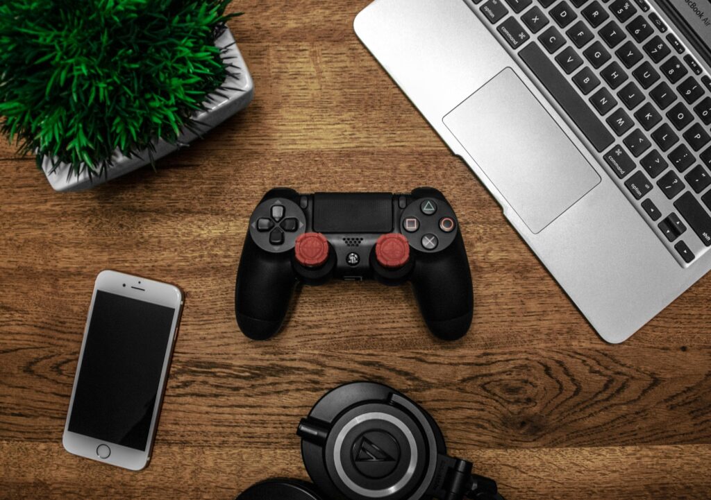 An arrangement of a laptop, phone, headphones, and gaming controller